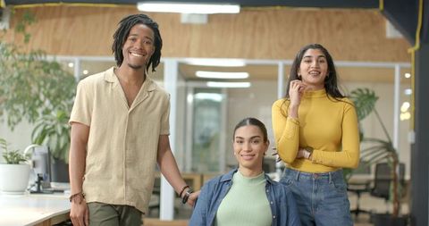 Smiling diverse startup team posing in modern open-plan office with plants and casual attire