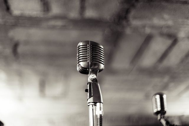 A close-up on a vintage microphone, placed on a stage, evokes nostalgia and classic musical performances. It is ideal for use in articles, blogs, and promotional materials related to music concerts, historical performances, audio equipment, and retro themes.