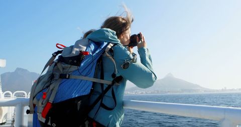 Woman Backpacker Photographing Ocean View from Boat with Mountains