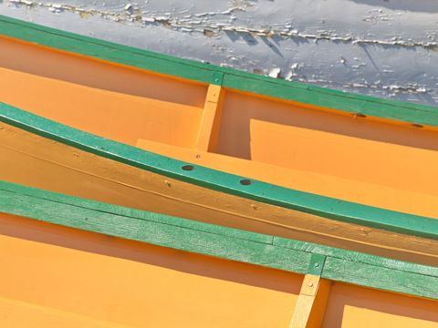 Vibrant orange and green wooden boats sitting overlapping with textured peeling paint
