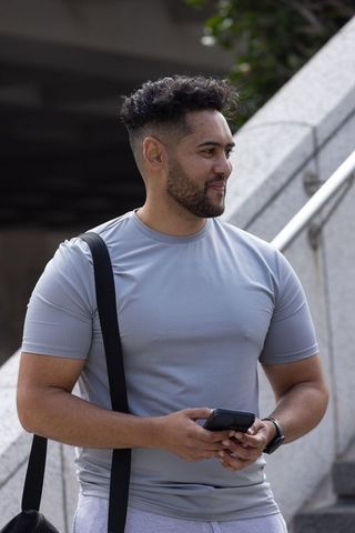 Urban fitness man standing on concrete steps holding smartphone and wearing smartwatch