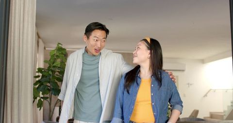 Diverse couple entering sunlit modern living room sharing warm smile and embrace