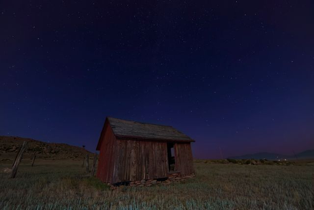 Depicts an old wooden shack in a rural area under a clear, starry night sky. Ideal for use in themes related to solitude, abandonment, rural life, and scenic night landscapes. Can be used for blog posts, travel websites, and backgrounds emphasizing peace and tranquility.