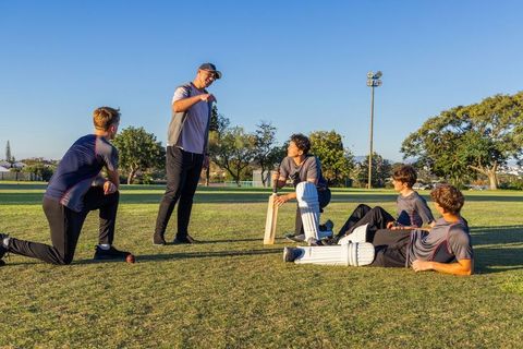 Diverse youth cricket team listening to coach on sunlit outfield during practice session