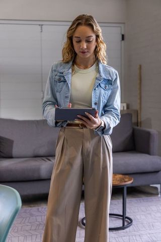 Young woman in modern lounge holding tablet wearing denim jacket and wide trousers