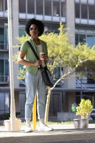 African american commuter standing with coffee and messenger bag outside urban office