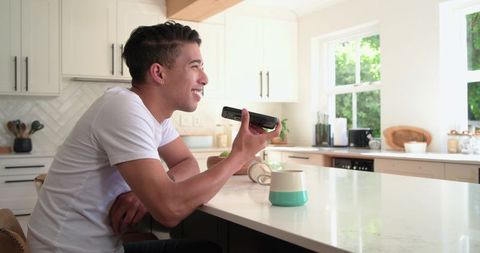 African american man talking on smartphone at bright kitchen island with teal mug