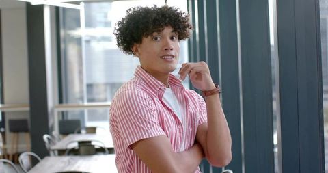 Confident young man standing in modern coworking lounge wearing pink-striped shirt