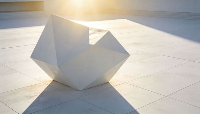 Minimalist White Polyhedral Sculpture Casting Long Geometric Shadows on Tiled Plaza