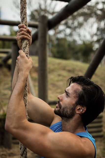 Determined man climbing a rope during obstacle course in boot camp