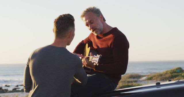 Man playing guitar by the beach with friend listening - Download Free Stock Images Pikwizard.com