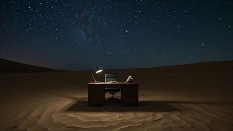 Surreal office desk in desert with starry night sky