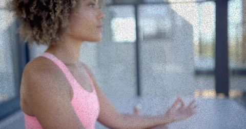 Woman meditating in sunlit yoga studio holding mudra breathing for mindful wellness