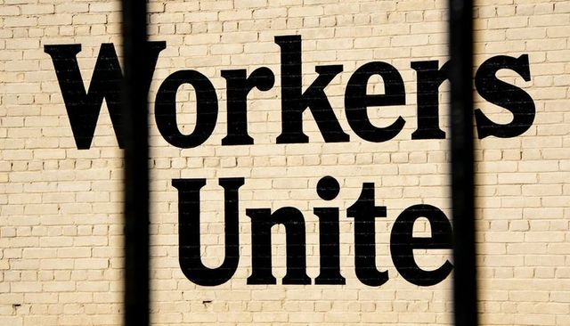 Workers unite mural on painted brick wall with dramatic shadowed bars urban protest serif