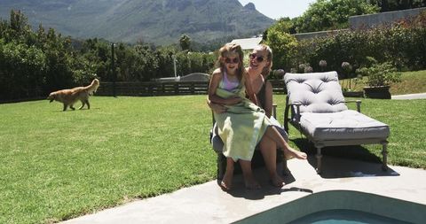 Mother and daughter relaxing poolside on lounge chair with dog in sunny backyard