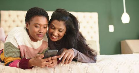 Diverse Female Couple Smiling Together at Home with Smartphone