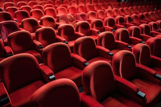 Rows of empty red seats fill a theater, awaiting an audience. The image captures the anticipation before a performance or movie screening.