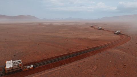 Convoy of track-laying machines laying parallel rails across red arid plain