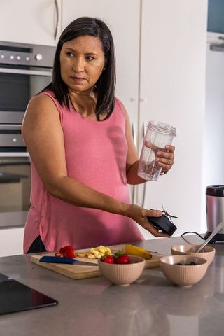 Mature woman preparing fruit smoothie in modern kitchen holding blender cup and blade