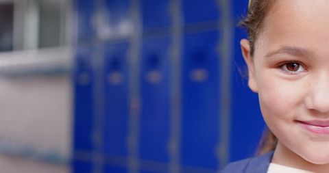 Smiling Schoolgirl Stands by Blue Lockers