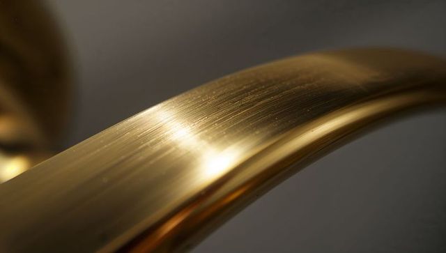 Curved brushed brass handle reflecting warm highlights and brushed metal texture