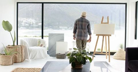 Indian artist contemplating blank canvas in coastal minimalist studio with waterfront view