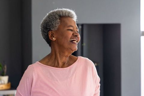 Joyful senior african american woman laughing in modern home wearing pink top portrait