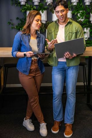Young diverse coworkers collaborating with laptop and tablet in modern lounge with plants