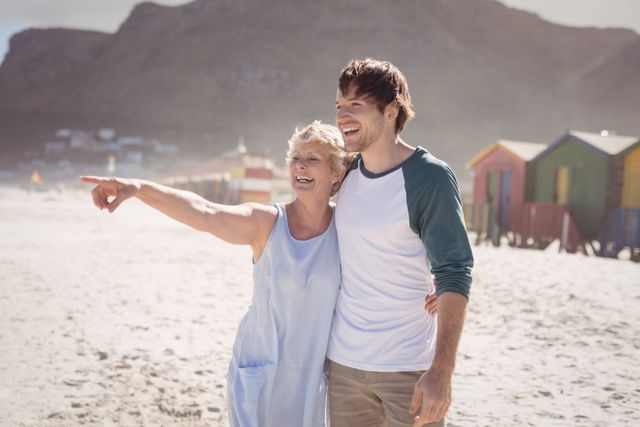 Happy woman pointing away with her son standing at beach during sunny day