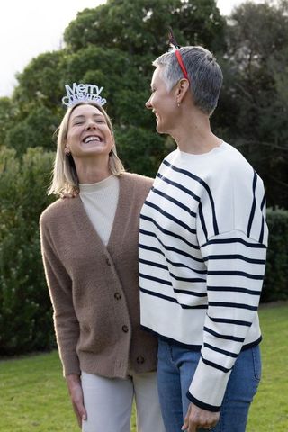 Female couple celebrating christmas outdoors laughing, wearing festive headbands