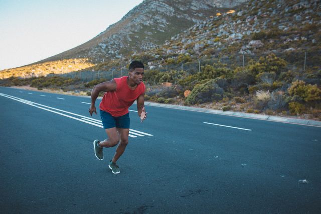 Man running on an empty coastal road near mountains, ideal for promoting outdoor fitness, healthy lifestyle, and athletic training. Suitable for use in fitness blogs, exercise programs, sportswear advertisements, and motivational content.
