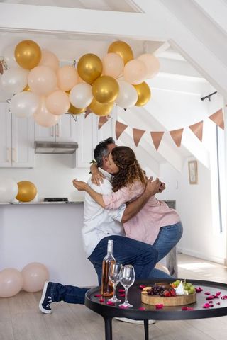 Couple embracing and celebrating with balloons and rose petals in modern kitchen
