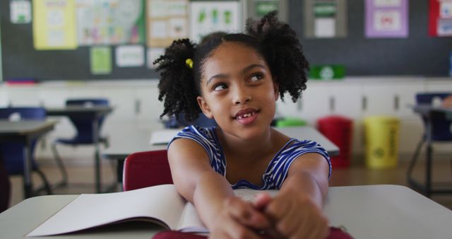 Young girl sitting in a classroom, smiling, and engaging in a learning activity. Perfect for educational content, school promotions, and children's learning programs.