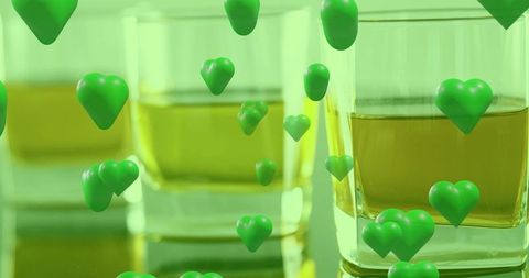 Floating green hearts hovering around golden tumblers on reflective glass surface