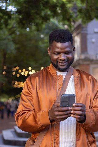 African american man checking phone under string lights on urban dusk walkway