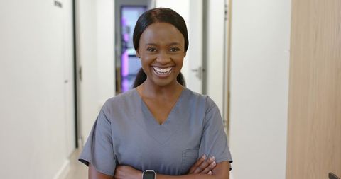 Confident healthcare professional smiling with arms crossed in modern clinic corridor