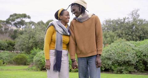 African American couple holding hands smiling in cozy autumn park wearing knit scarves