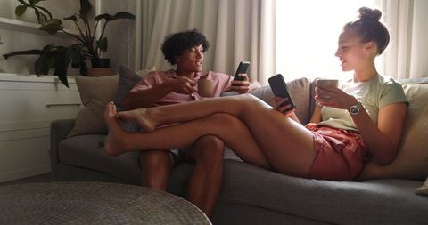 Couple Relaxing on Couch with Smartphones and Mugs in Cozy Living Room