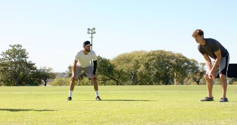 Two teammates holding defensive stance during outdoor football training on sunny grass field