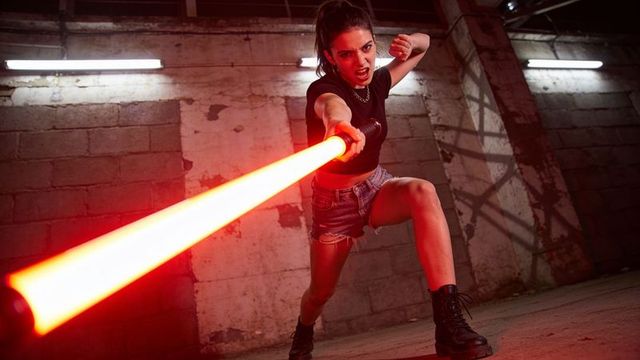 Lunging female warrior wielding glowing red energy saber in gritty industrial space