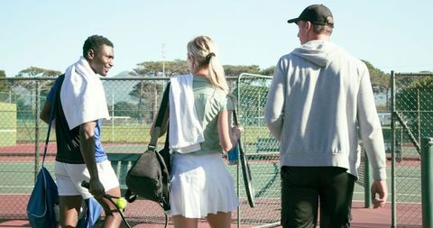 Group of friends walking from tennis court carrying rackets and towels on sunny day