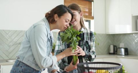 Multicultural women smelling fresh celery while preparing meal at modern kitchen counter