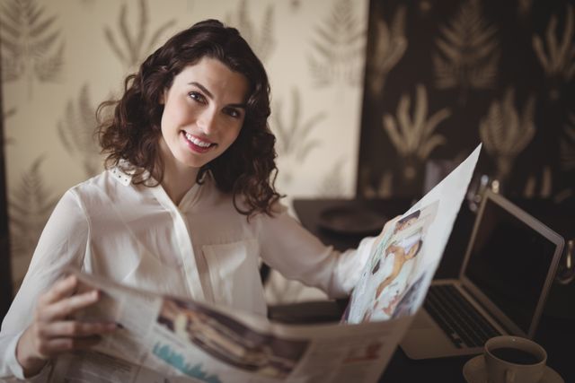 Young woman enjoying a relaxing moment in a cafe while reading a newspaper. Ideal for use in lifestyle blogs, articles about relaxation, or advertisements for cafes and restaurants.