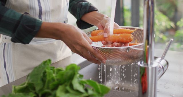 Hands washing fresh carrots under running water in kitchen sink, ideal for healthy eating, home cooking, meal preparation, nutrition, and cleanliness concepts. Could be used in cooking blogs, recipe websites, or advertisements promoting fresh produce.