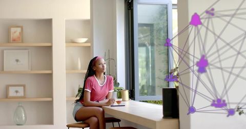 Young woman relaxing by open window holding mug beside smart speaker in bright minimalist kitchen
