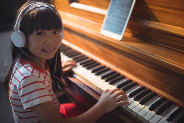 High angle portrait of girl wearing headphones while practicing piano in classroom at music school