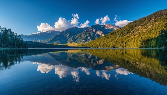 Sunlit alpine mountain range reflecting on glassy lake in conifer forest valley at dawn