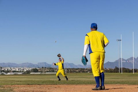 Outfielders in yellow uniforms catching fly ball on sunny suburban baseball field