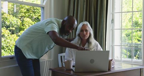 Diverse couple collaborating on laptop at home for work discussion