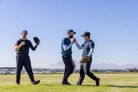 Male Baseball Teammates Celebrating with Fist Bump on Community Field Wearing Gloves